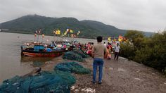 there are many people standing on the shore next to fishing nets and boats in the water