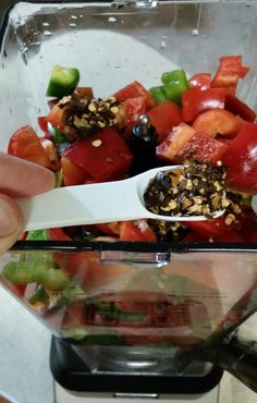 a person holding a spoon in a blender full of fruit and vegetables with nuts