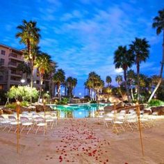 an empty pool surrounded by palm trees and lawn chairs with lights on them at night