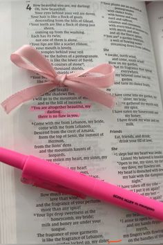 a pink pen sitting on top of an open book next to a pink ribbon tied around it