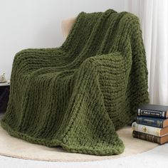 a green knitted blanket sitting on top of a chair next to two books and a lamp