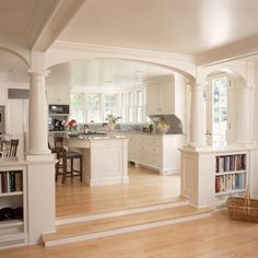 an open kitchen and dining room with white cabinets, wood floors and bookcases