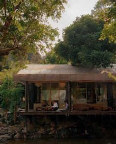 two people sitting on the porch of a house next to a body of water with trees in the background