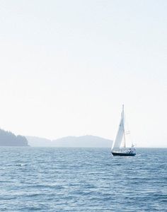 a sailboat sailing on the ocean with mountains in the background