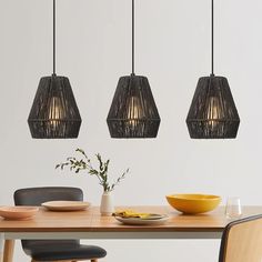 three pendant lights hanging over a table with plates and bowls on it, along with a vase filled with flowers