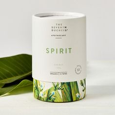 a white cup sitting on top of a table next to a green leafy plant