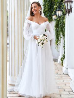 a woman in a white wedding gown standing on a brick walkway with columns and greenery behind her