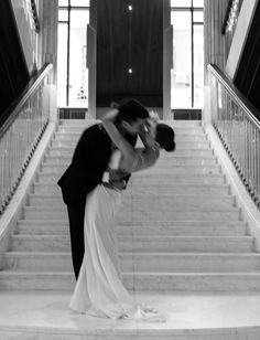 a bride and groom kissing in front of the staircases at their wedding reception, black and white photograph