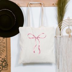 a white tote bag with a pink bow on it next to a straw hat