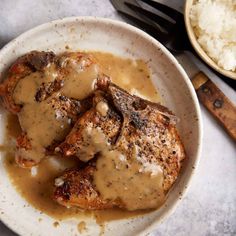 two pieces of meat covered in gravy on a white plate next to rice