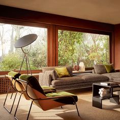 a living room filled with lots of furniture and large windows covered in trees behind it