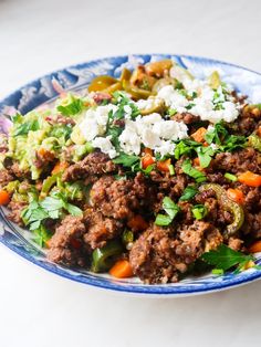 a blue and white bowl filled with meat, vegetables and feta cheese on top