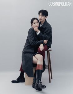 a man and woman sitting next to each other on top of a wooden chair in front of a gray background