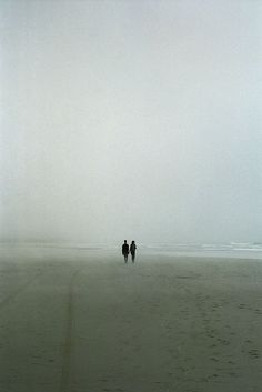 two people are walking along the beach on a foggy day