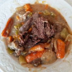 a white plate topped with meat and veggies covered in gravy on top of a table