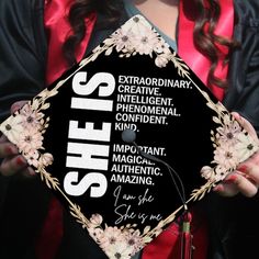 a woman in graduation gown holding up a black and white hat with she's written on it