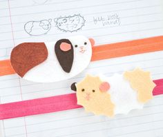 two felt animals are sitting on top of a piece of lined paper with pencils