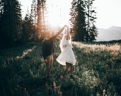 a man and woman are dancing in the grass with their hands up to each other