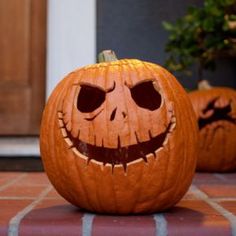 two carved pumpkins sitting on top of a tiled floor next to a planter