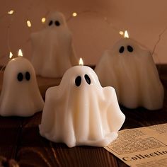 three white ghost candles sitting on top of a wooden table next to a piece of paper