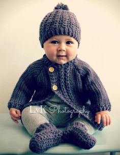 a baby sitting on top of a blue table wearing a knitted sweater and hat