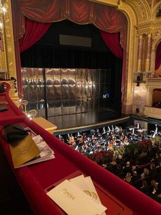 an auditorium filled with lots of people sitting on red seats and looking at the stage