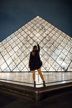 a woman standing in front of the pyramid at night with her hand up to the sky