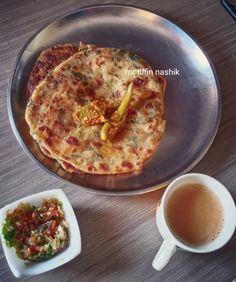 two small pizzas on a metal plate next to a cup of coffee and saucer