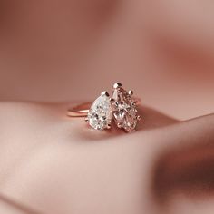 two pear shaped diamond engagement rings sitting on top of a pink satin material surface,