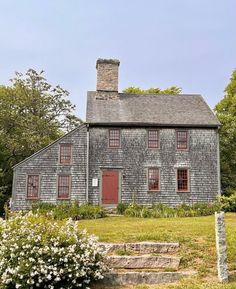 an old gray house with red windows and steps leading up to the front door on a sunny day