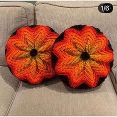 two orange crocheted flower cushions sitting on top of a gray couch next to each other