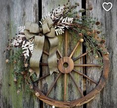 an old wagon wheel decorated with pine cones and greenery is hung on the side of a wooden fence