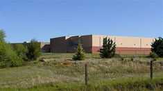 an industrial building sits in the middle of a field with tall grass and trees around it