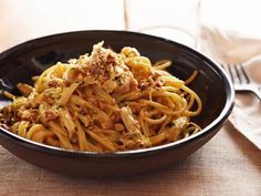 a black bowl filled with pasta and meat on top of a table next to a fork