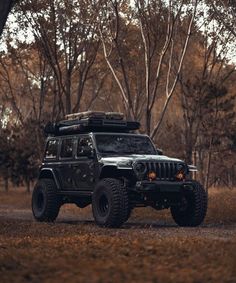 a black jeep parked on the side of a dirt road in front of some trees