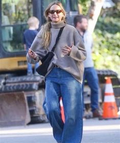 a woman walking down the street with her hand in her pocket and wearing jeans, a turtle neck sweater and black booties