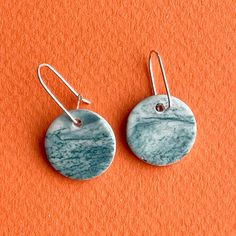 pair of earrings on an orange background with silver earwires and small round disc