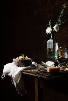 a table with food and flowers in a glass vase on it, next to a bottle of wine