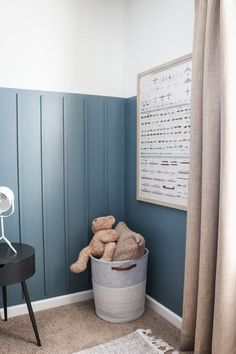 a teddy bear is sitting in a bucket next to a lamp and a poster on the wall