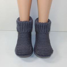 a doll's feet wearing gray knitted slippers and socks on a white surface