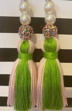 two green tassels with pearls and beads hanging from the end of each ear