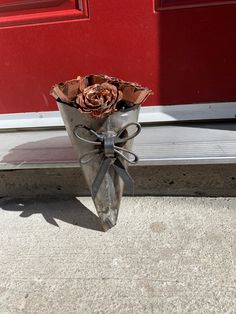 a metal vase with flowers in it sitting on the ground next to a red door