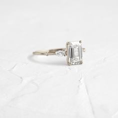 an emerald cut diamond engagement ring on a white background