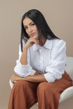 a woman sitting in a chair with her hand on her chin and looking at the camera