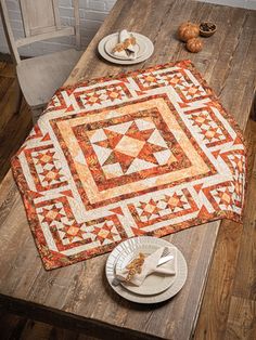 an orange and white quilt sitting on top of a wooden table next to two plates