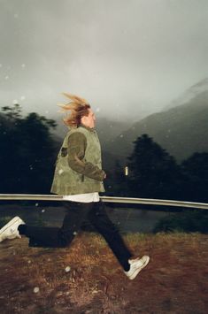 a woman running in the rain with her hair blowing in the wind and mountains behind her