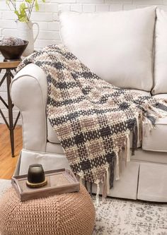 a living room with a couch, ottoman and rug on the floor in front of a white brick wall