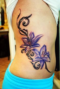 a woman's lower back tattoo with purple flowers and swirls on the side