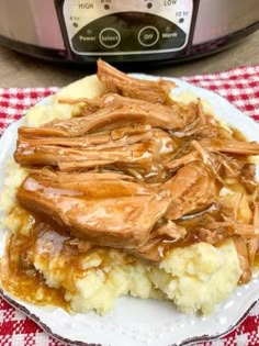 a plate topped with meat and potatoes next to an instant pot roaster on a red checkered tablecloth