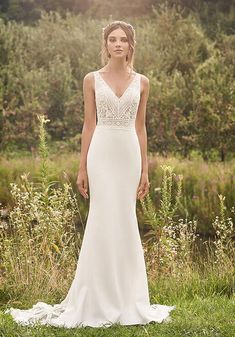 a woman in a white wedding dress standing on grass with trees and bushes behind her